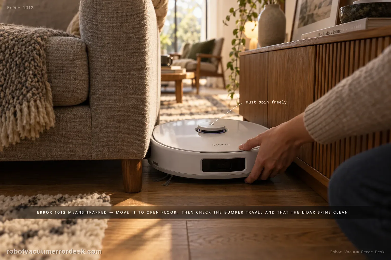 Narwal Freo Z Ultra wedged in a tight gap between a sofa leg and a low cabinet on oak flooring with a hand reaching in to lift it toward open floor, captioned that Error 1012 means trapped: move it to open floor, then check the bumper travel and that the LiDAR spins clean.