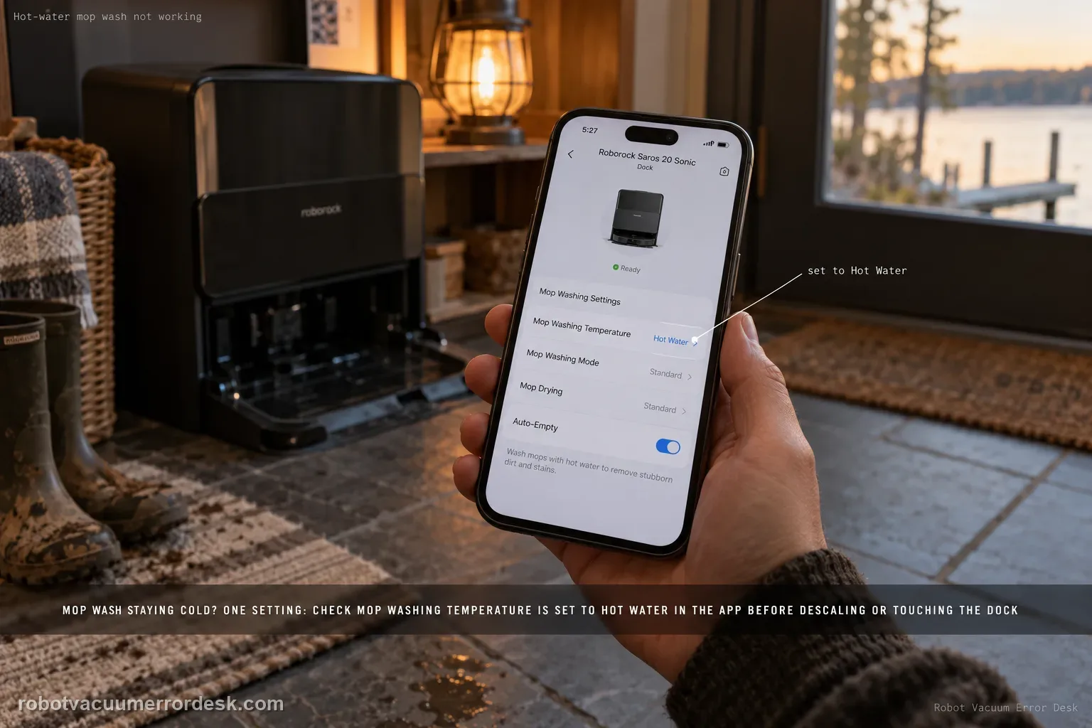 A hand holding a phone showing the Roborock app mop-wash settings beside a Saros 20 Sonic dock in warm lamp light.